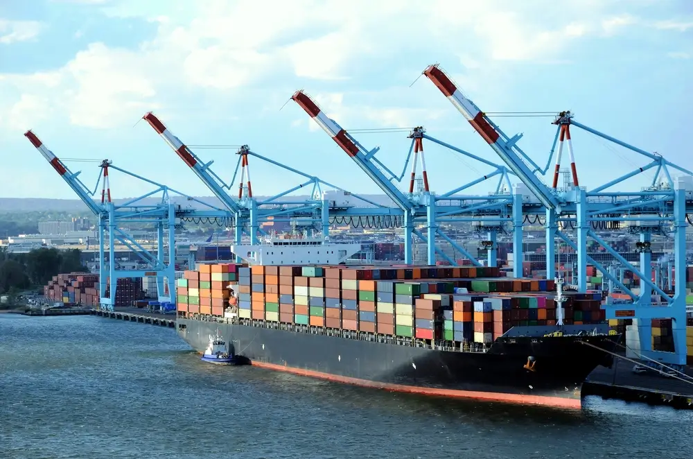 A large cargo ship loaded with containers docked at a port equipped with modern cranes